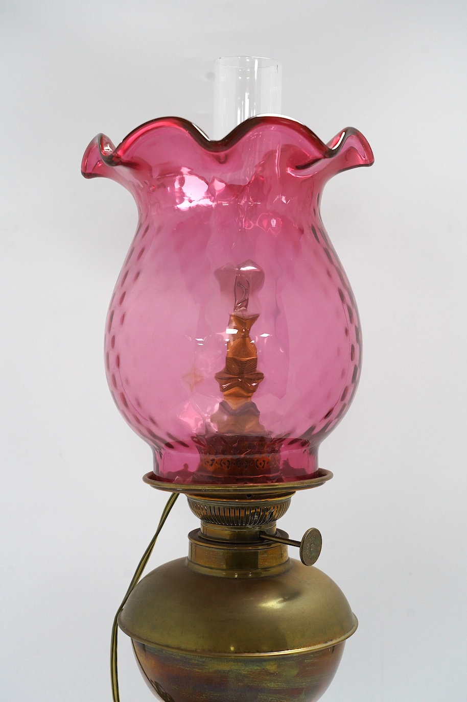 A Victorian brass oil lamp with cranberry glass shade. Condition - fair